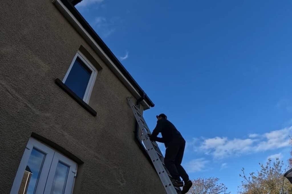 A technician climbing a ladder to inspect and repair gutters on a two-story home in New Jersey – gutter repair NJ by A1 Oasis Construction LLC.